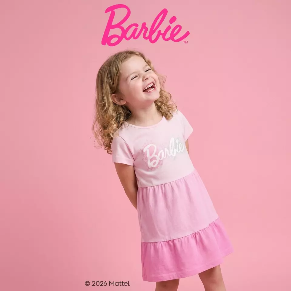 Niña sonriente con vestido rosa de Barbie de Pepco con volantes en tonos degradados.