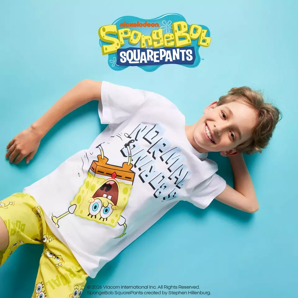 Chłopiec w białej koszulce Pepco z nadrukiem SpongeBob SquarePants leży uśmiechnięty na turkusowym tle.