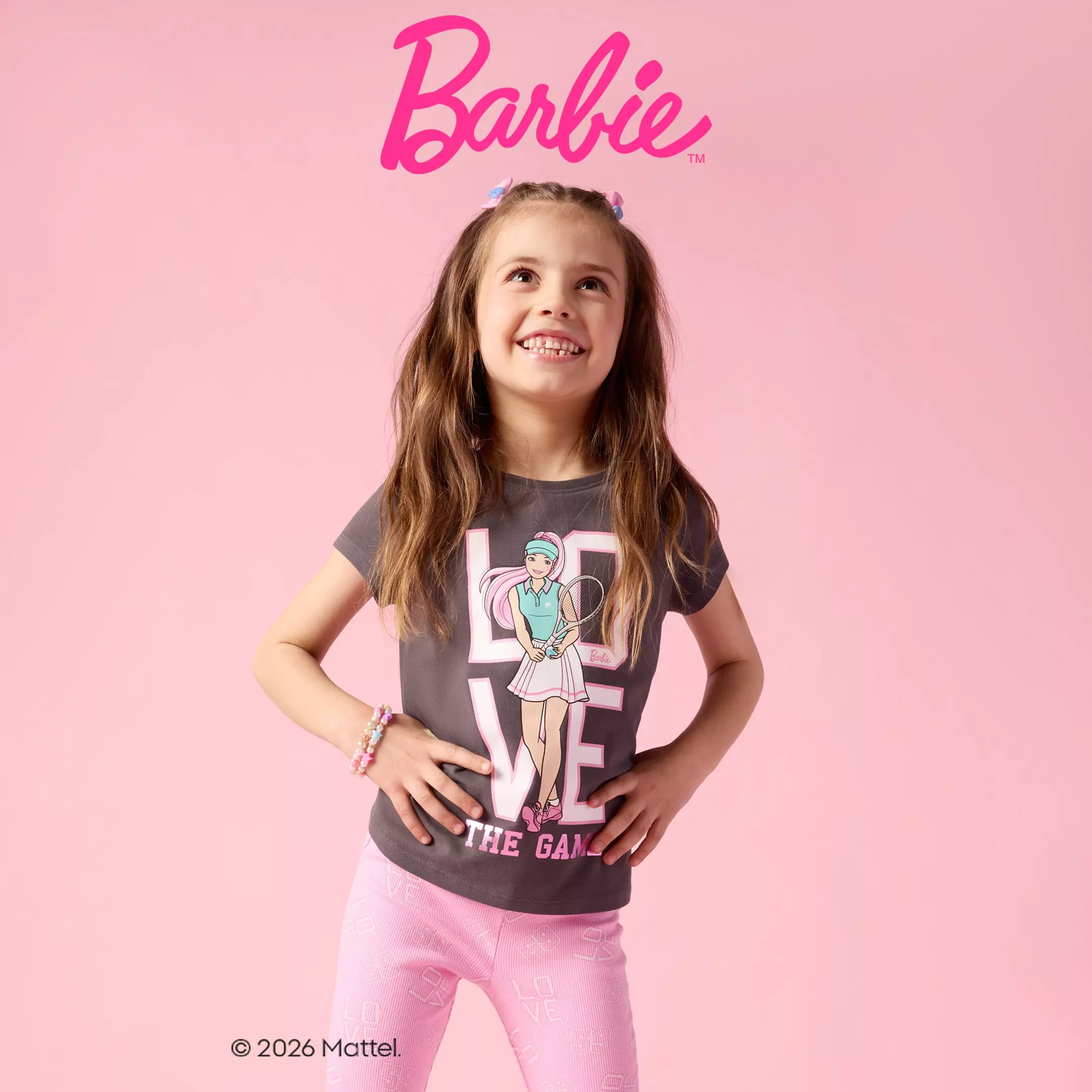 Uśmiechnięta dziewczynka w szarej koszulce Barbie i różowych spodniach od Pepco.