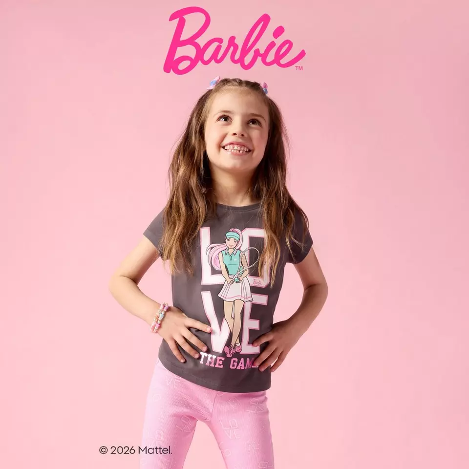 Uśmiechnięta dziewczynka w szarej koszulce Barbie i różowych spodniach od Pepco.