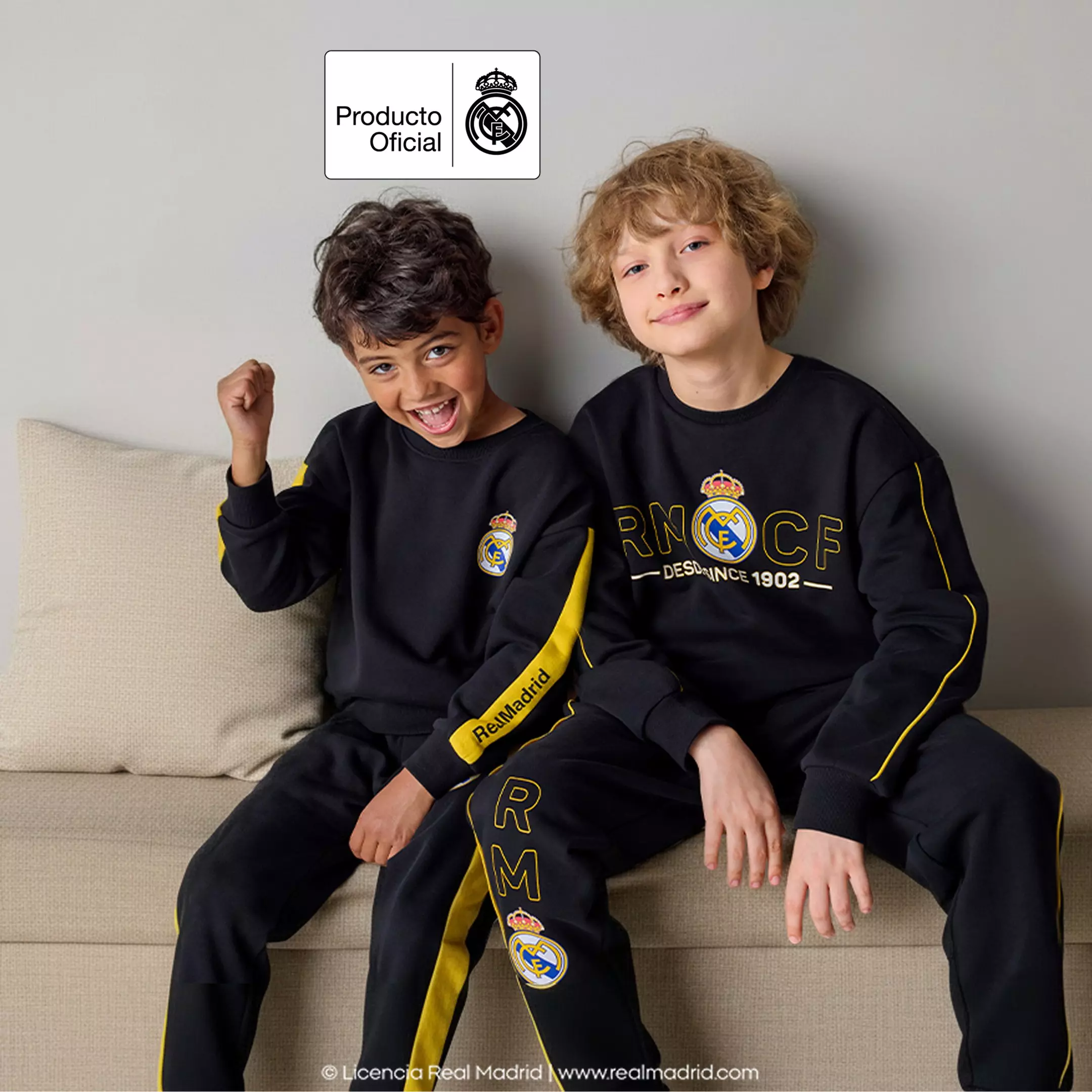 Dva chlapci v černých teplákovách souprávách Pepco s logem Real Madrid sedí na pohovce a usmívají se.