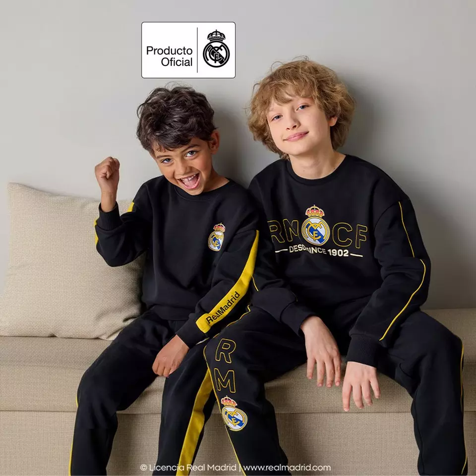 Dva chlapci v černých teplákovách souprávách Pepco s logem Real Madrid sedí na pohovce a usmívají se.