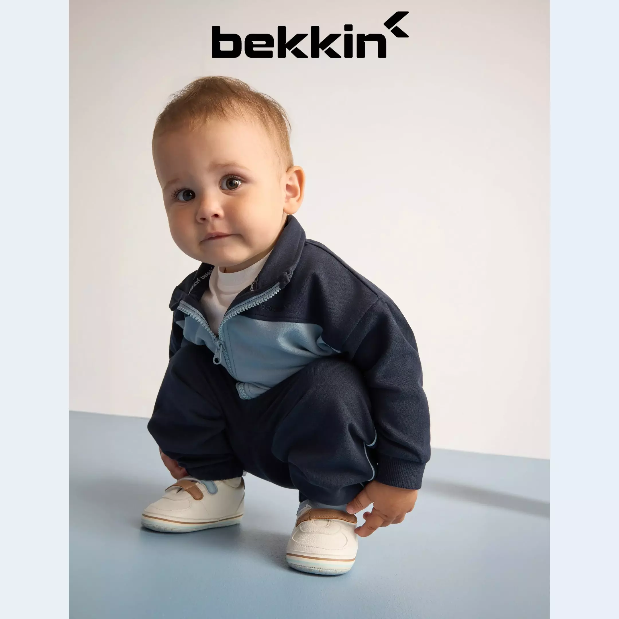 Pepco - Bebeluș purtând jachetă bleumarin bekkin și adidași bej, ghemuindu-se și zâmbind.