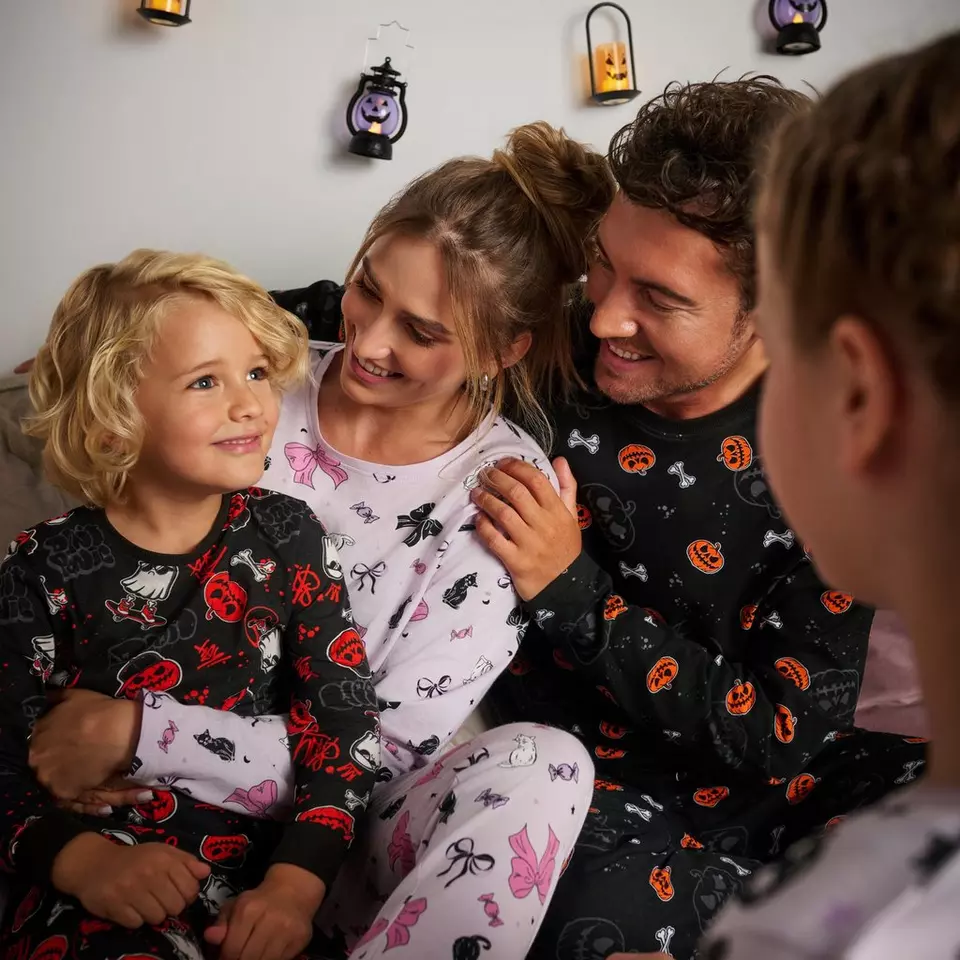 Famiglia Pepco che indossa pigiami coordinati a tema Halloween con decorazioni festive appese al muro.