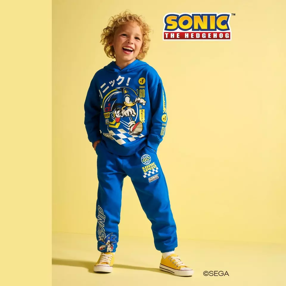 Chlapec se směje v modré teplákovém soupravě Pepco s potiskem Sonic the Hedgehog.