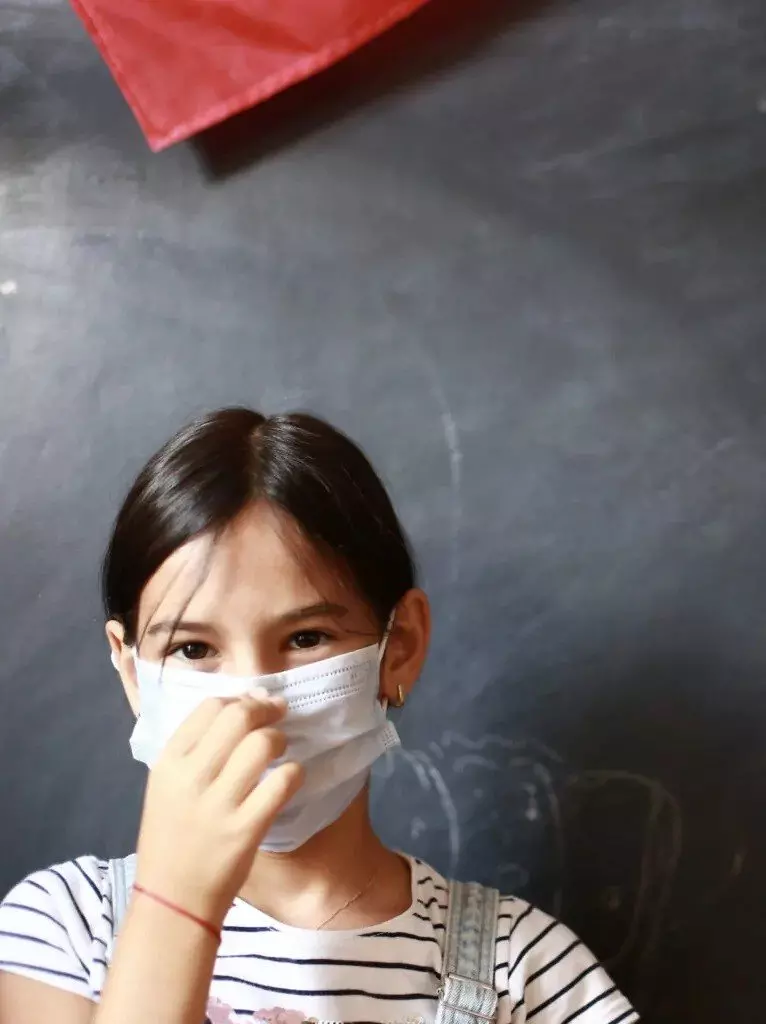 Fată cu păr șaten purtând o mască facială albă și un tricou în dungi.