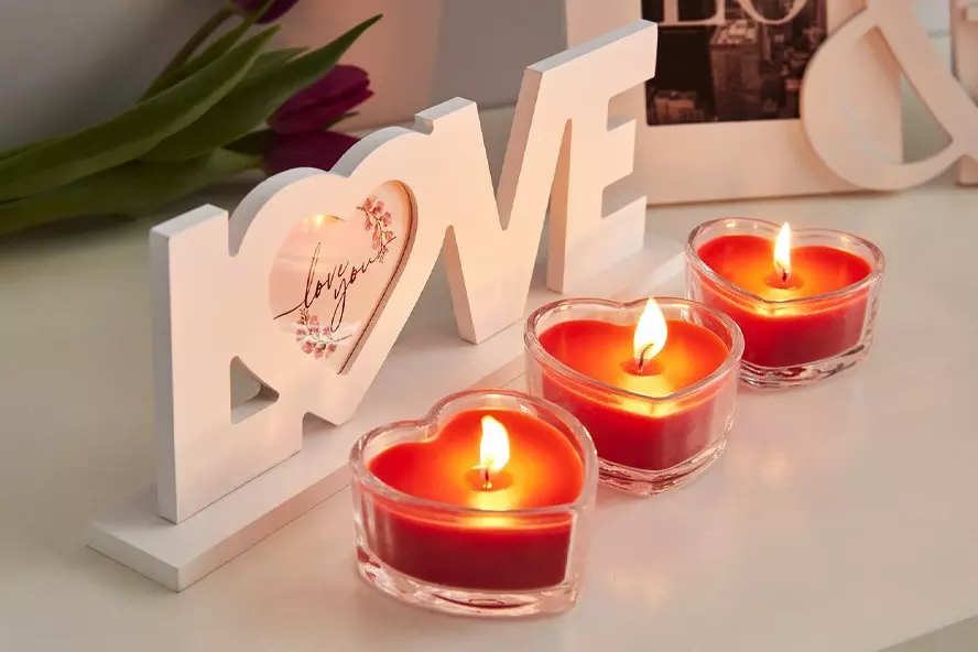 Biała dekoracja LOVE z Pepco z napisem love you oraz trzy czerwone świeczki w kształcie serca z płomieniami.