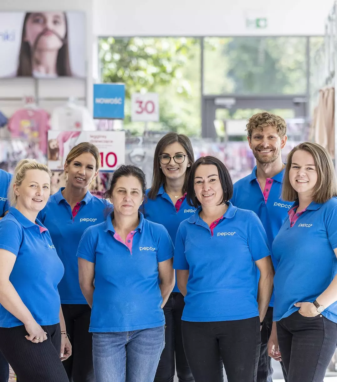 Pepco store staff wearing blue company uniforms with pink accents standing together in a retail environment with promotional signs.