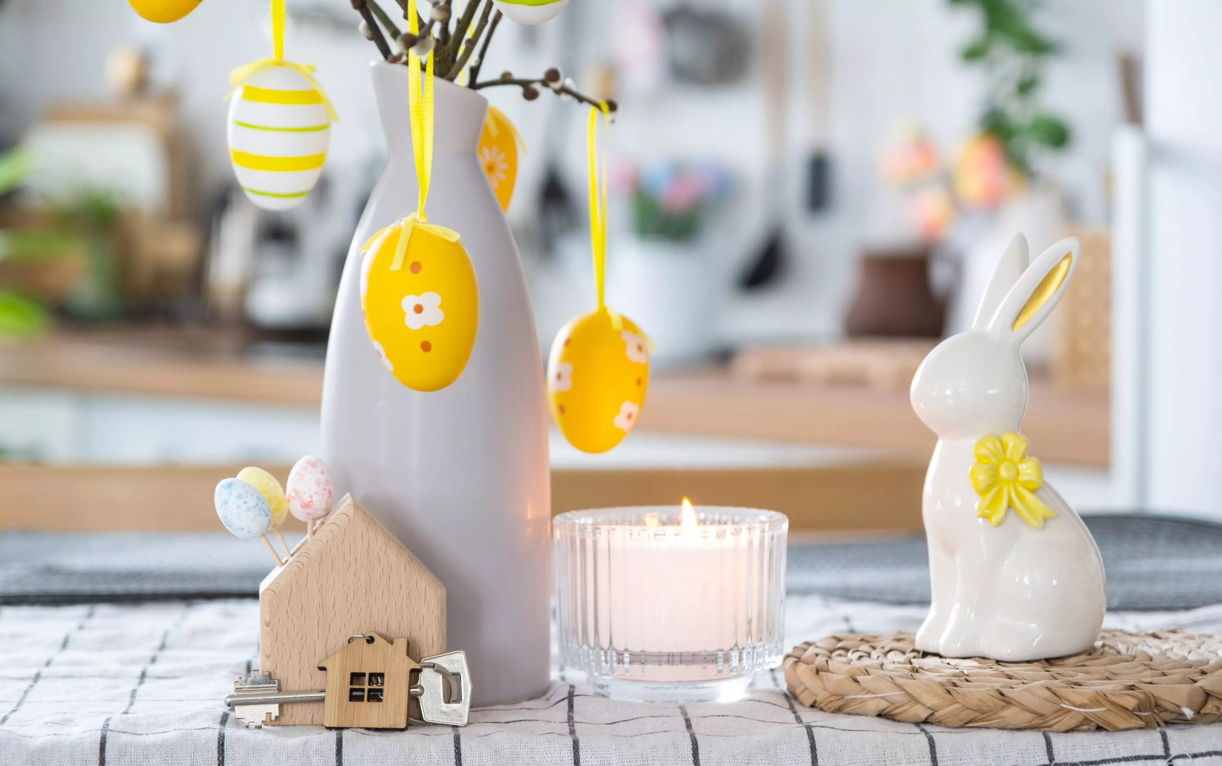 Decorazioni pasquali Pepco con uova gialle appese, coniglietto bianco in ceramica e candela profumata.