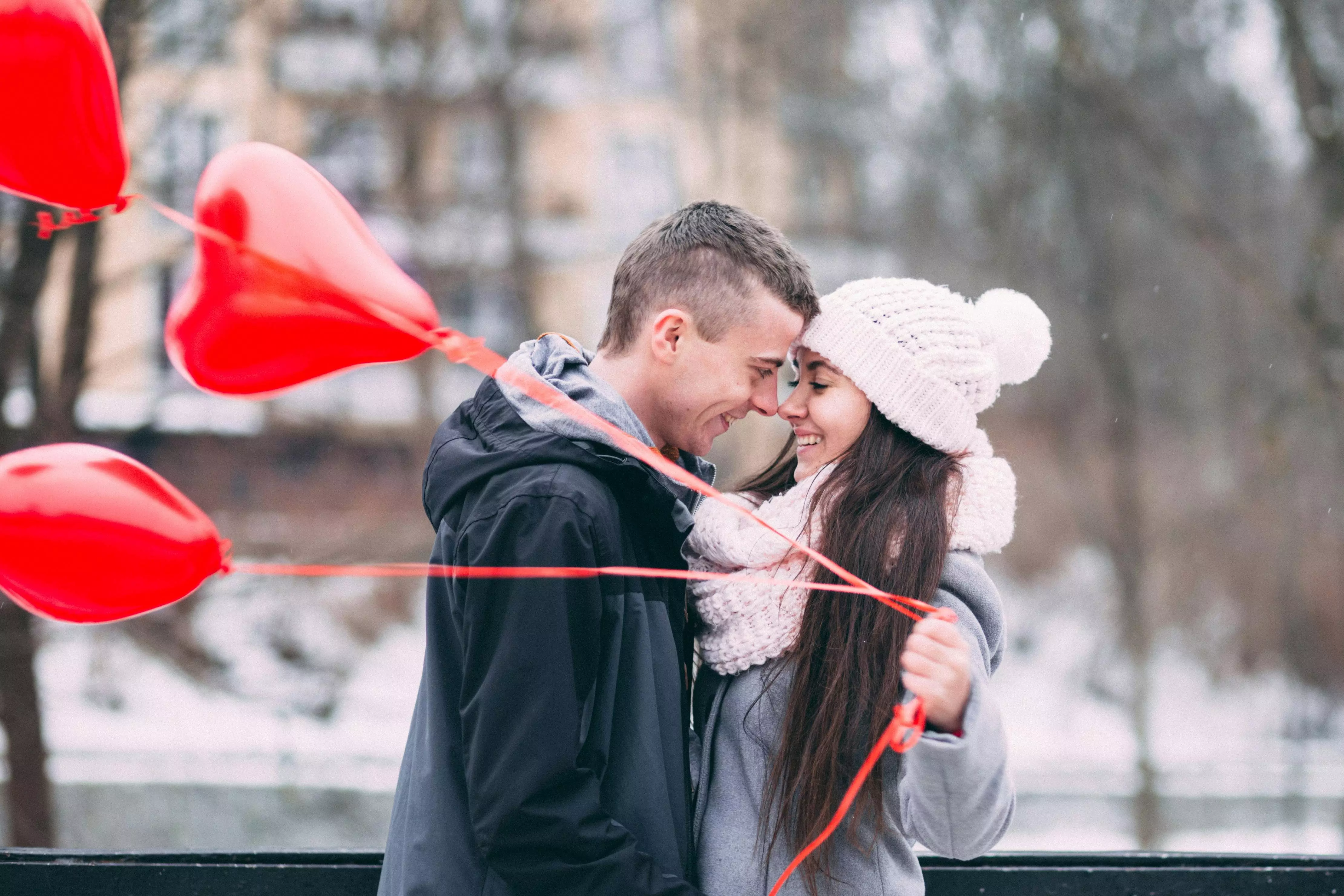 Coppia che si abbraccia all'aperto con palloncini a cuore rossi Pepco in una giornata invernale romantica.