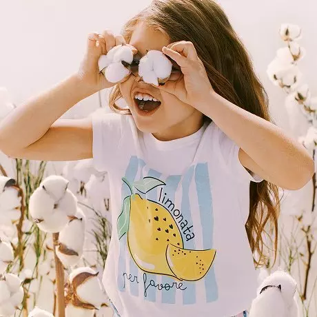 Niña sonriente sostiene flores blancas sobre sus ojos con camiseta de limonada.