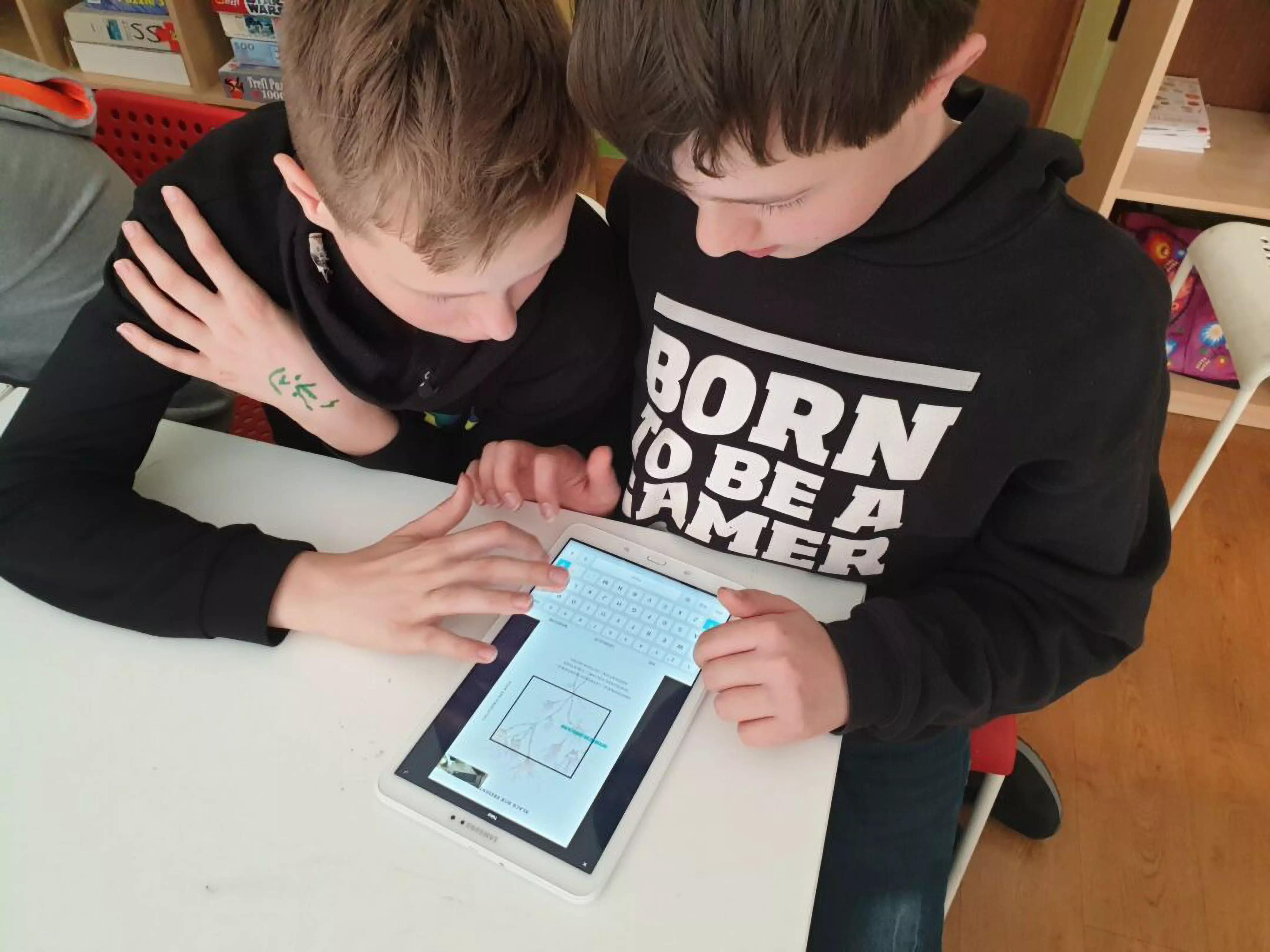 Dwoje dzieci w czarnych bluzach Pepco wspólnie korzysta z tabletu przy białym stoliku w klasie.