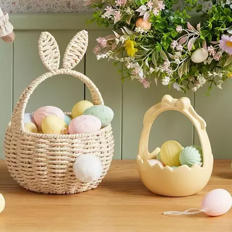 Wiklinowy koszyk z uszami królika i żółty koszyk wypełnione kolorowymi jajkami wielkanocnymi.