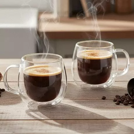 Dwie parujące filiżanki z podwójnymi ściankami z gorącą kawą od Pepco na drewnianym stole z ziarnami kawy.