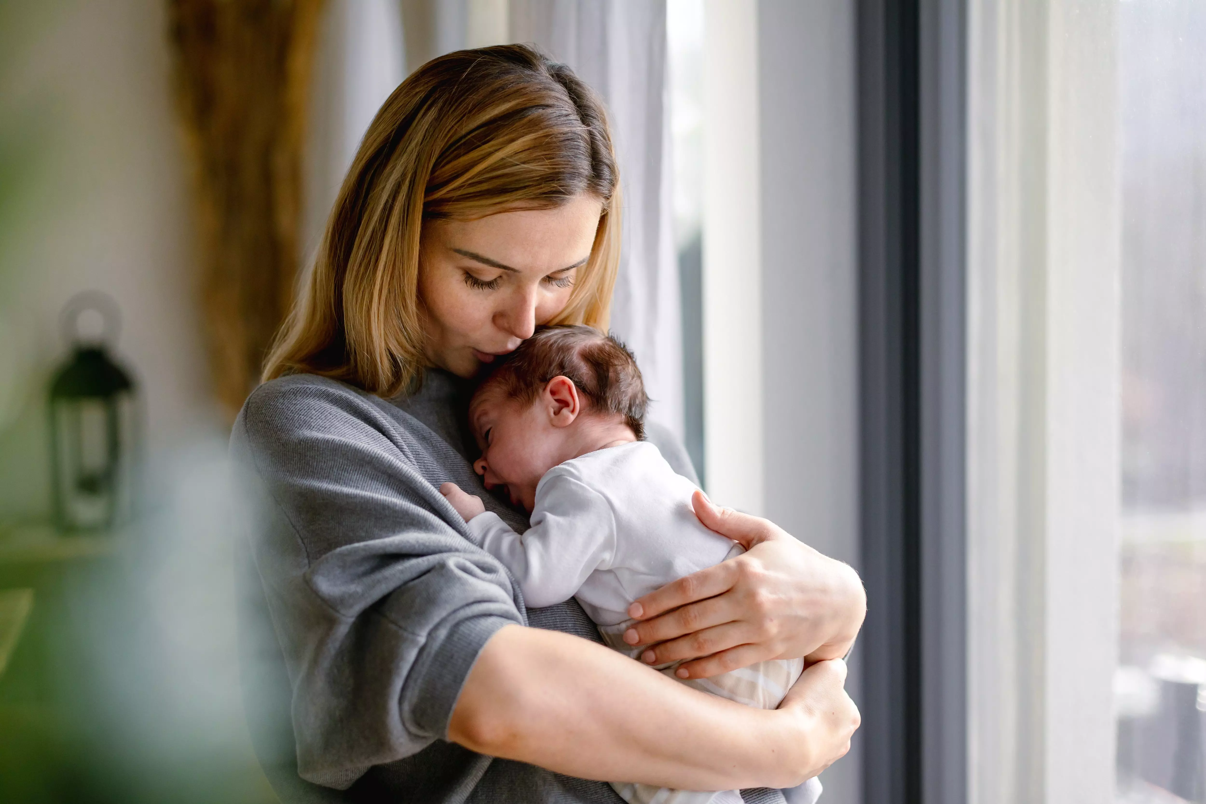 Mother tenderly holding and cuddling newborn baby at home in Pepco clothing.