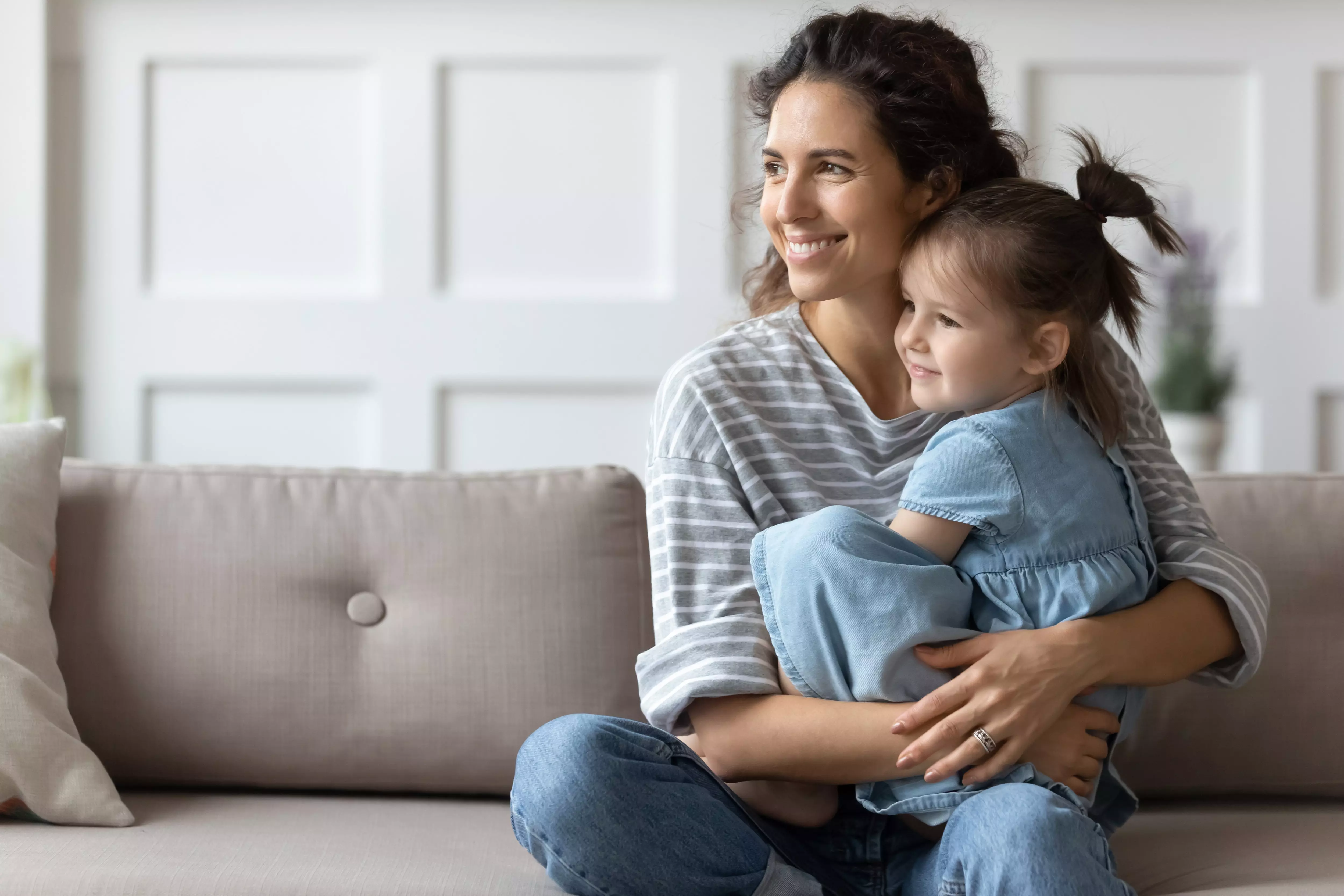 Pepco mother and daughter embracing on sofa, both smiling and wearing casual striped and denim clothing.