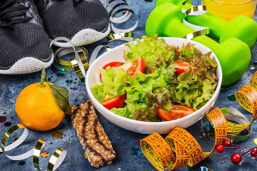 Pepco fitness scene with fresh salad, sports shoes, green dumbbells, orange, granola bar and measuring tape for healthy lifestyle.