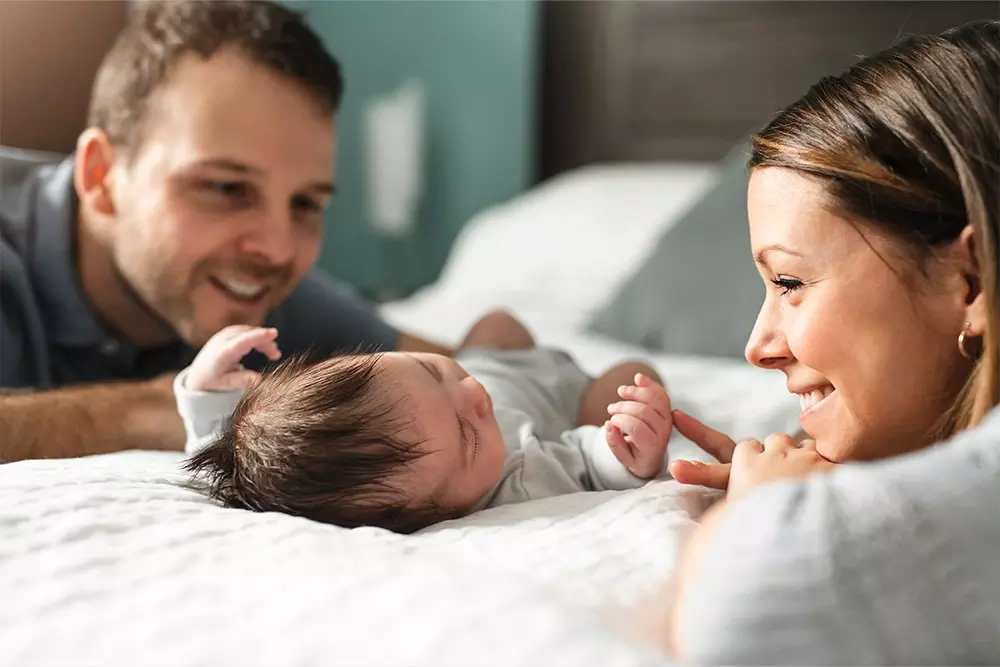 Padres sonrientes observando a su bebé recién nacido acostado en la cama.