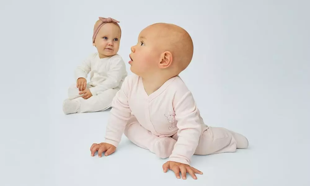 Niemowlęta w ubranku Pepco - jedno w różowym, drugie w białym śpioszku z opaską na głowie.