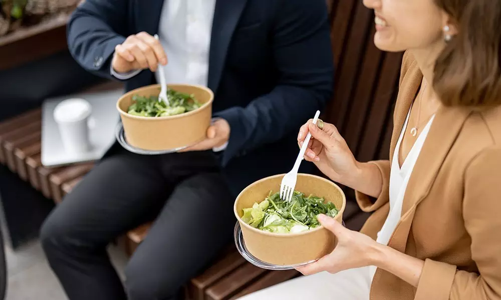 Dwie osoby jedzące sałatki z ekologicznych pojemników na lunch, używając sztućców Pepco podczas przerwy na posiłek.