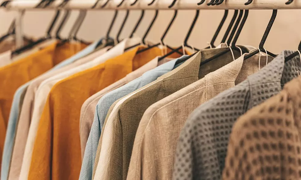 Kolekcja ubrań Pepco na wieszakach w odcieniach pomarańczowych, niebieskich i neutralnych, z widocznymi różnymi fakturami tkanin.