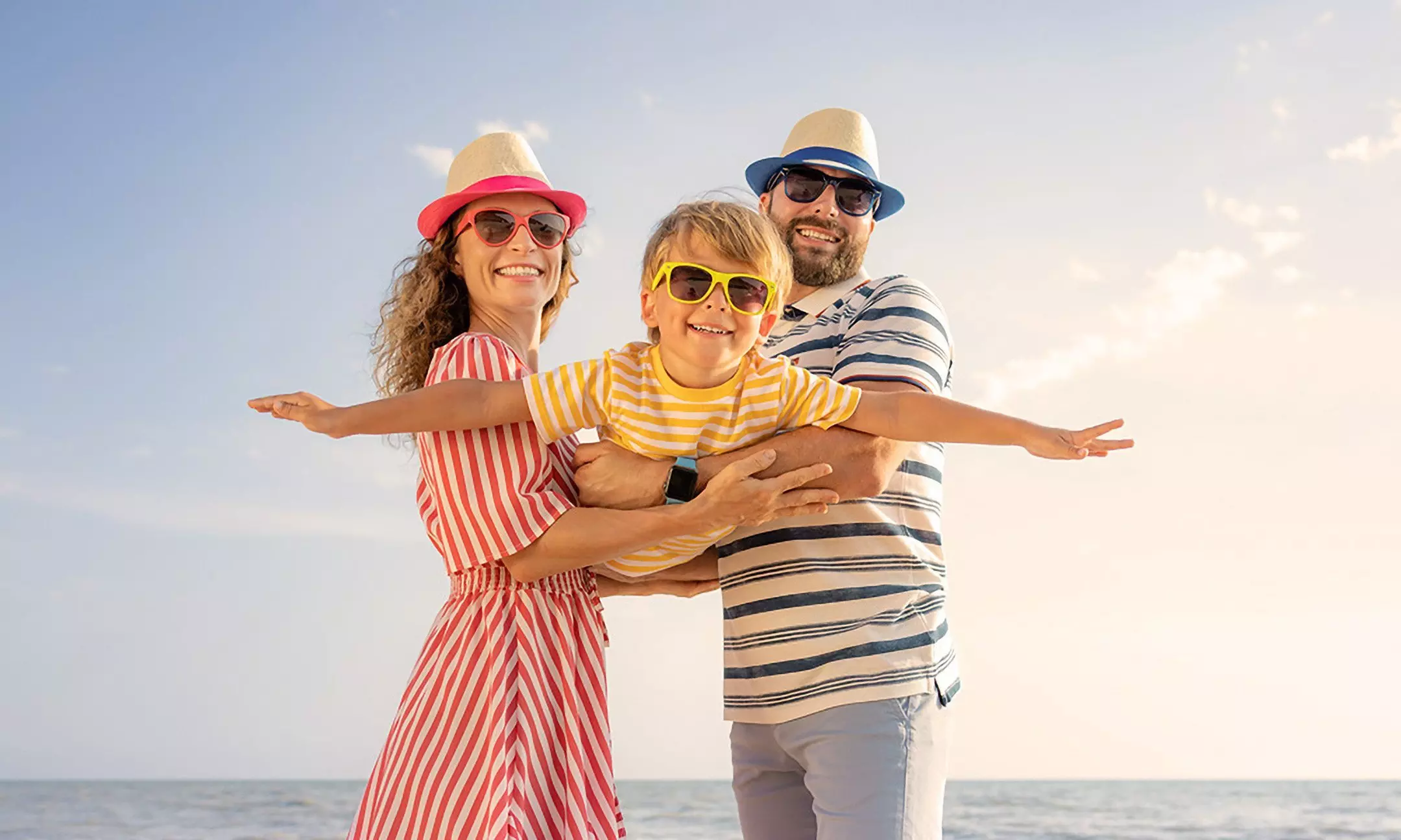 Rodzina w letniej odzieży Pepco - kapelusze i okulary przeciwsłoneczne, pozująca radośnie na plaży podczas wakacji.