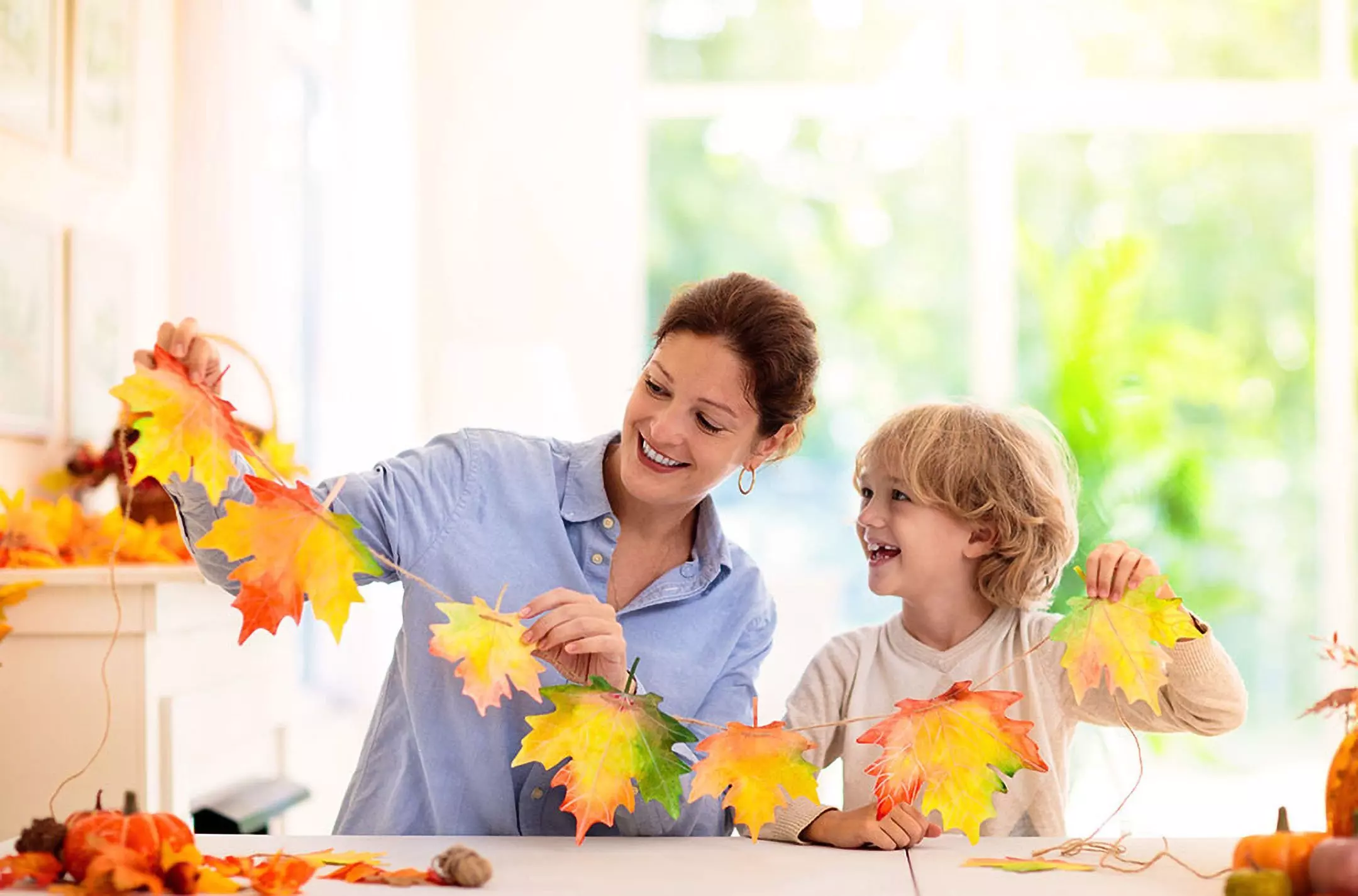 Kobieta i dziecko tworzą jesienną girlandę z kolorowych liści klonu od Pepco, uśmiechając się podczas wspólnego zajęcia.