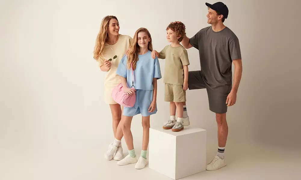 Família a usar conjuntos casuais Pepco em tons pastel e neutros, posando juntos num estúdio.