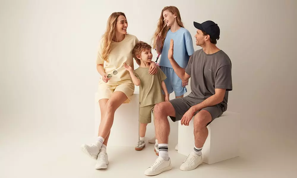 Family of four wearing matching casual loungewear sets in neutral tones, smiling and interacting together.