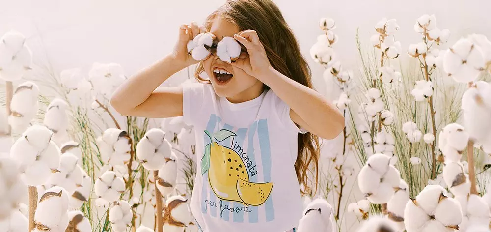 Niña sonriente de Pepco sosteniendo flores de algodón sobre sus ojos entre plantas de algodón.