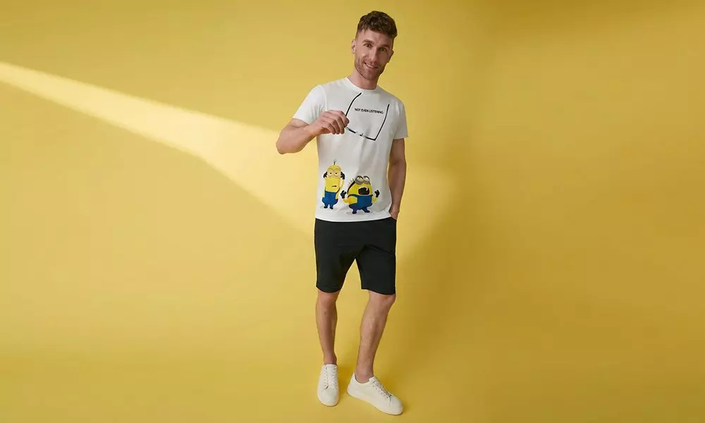 Man wearing Pepco white Minions t-shirt and black shorts holding sunglasses.
