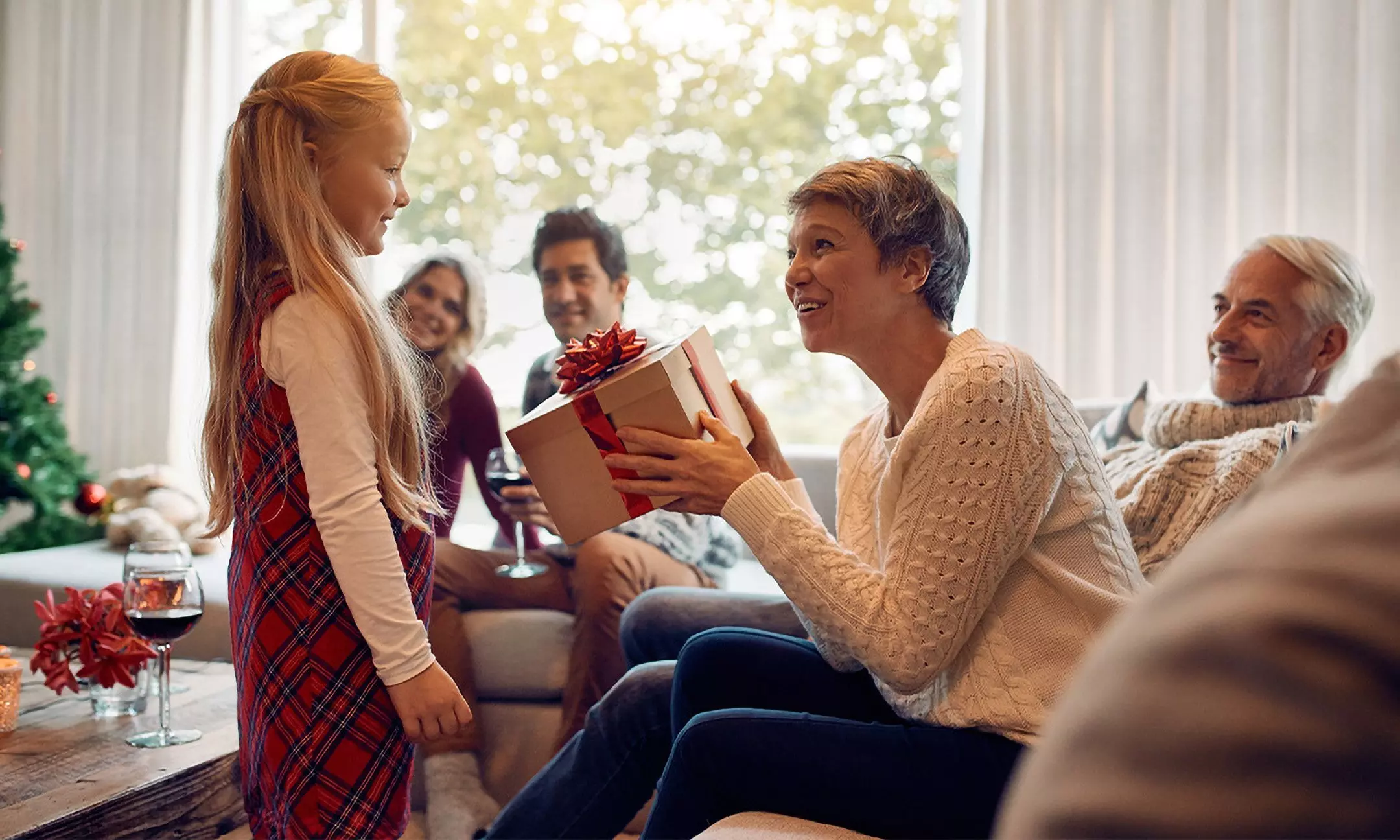 Rodzina świętuje Boże Narodzenie w domu, dziewczynka wręcza prezent od Pepco osobie w kremowym swetrze.
