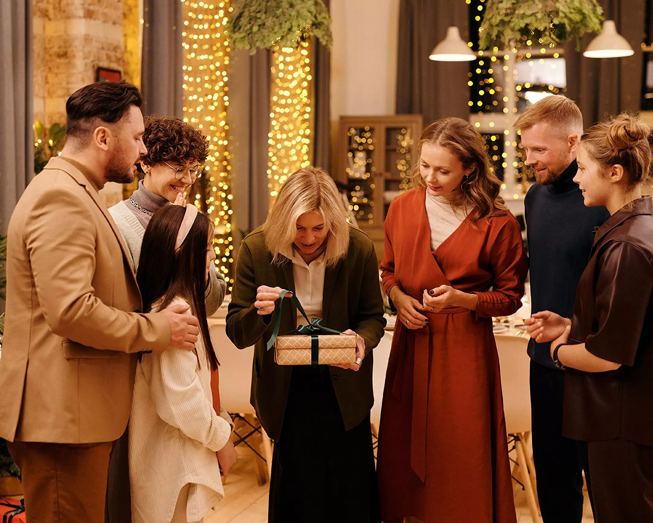 Grupa osób otwiera prezent świąteczny w przytulnym wnętrzu z dekoracjami świetlnymi Pepco w tle.