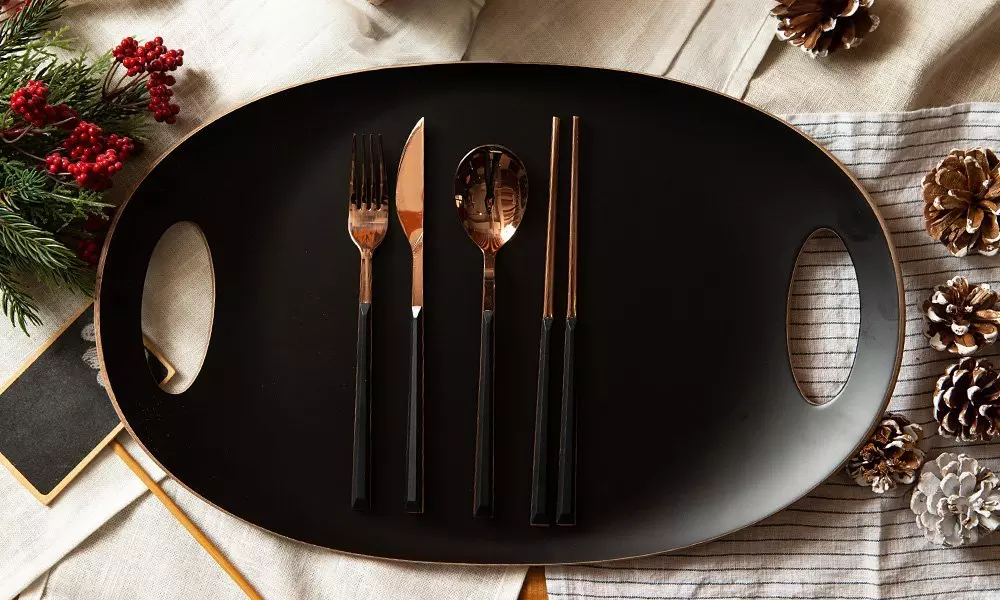 Elegancka czarna taca Pepco ze złotą obwódką i sztućcami w kolorze różowego złota, otoczona świątecznymi dekoracjami.