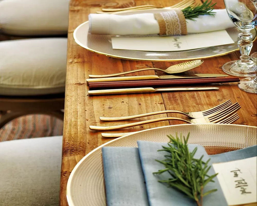 Elegancki stół z zastawą Pepco, złotymi sztućcami, serwetkami ozdobionymi gałązkami rozmarynu i karteczkami na talerzach.