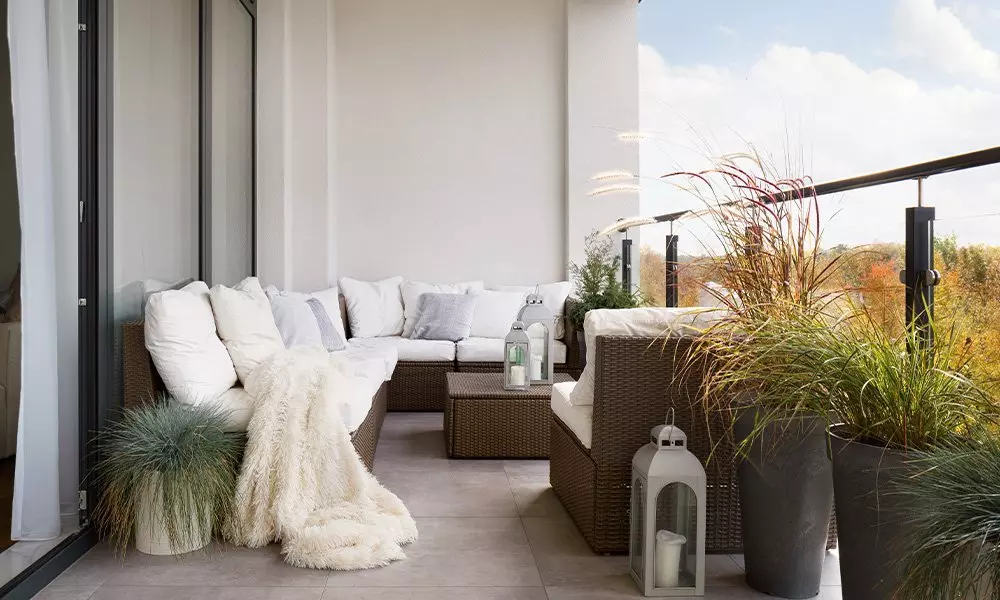 Pepco outdoor furniture set on a balcony with wicker seating, white cushions, decorative lanterns and ornamental grasses in planters.