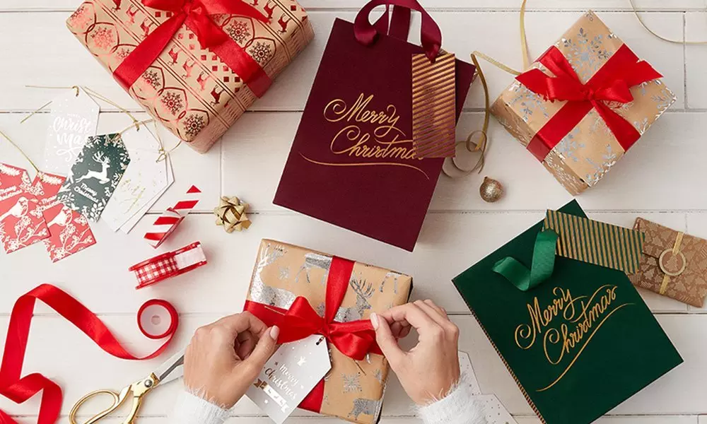 Pepco Christmas gift wrapping with hands tying red ribbon on present, surrounded by festive gift bags, wrapped packages and ribbon.