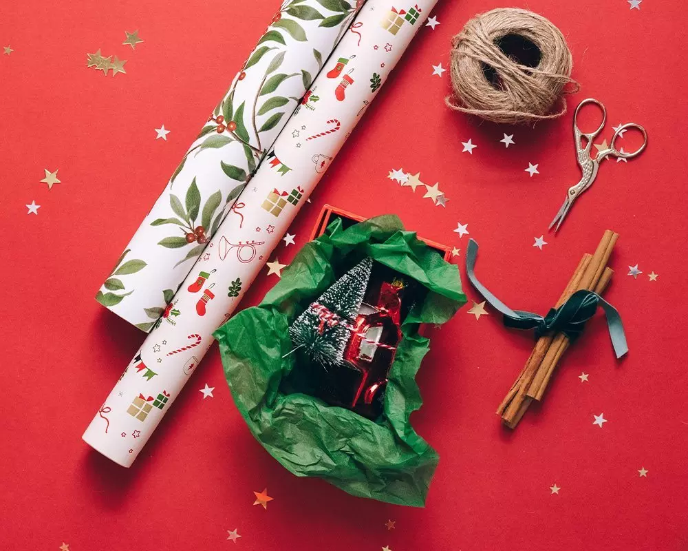 Pepco Christmas gift wrapping supplies with festive paper rolls, twine, scissors, cinnamon sticks, and a miniature tree decoration.
