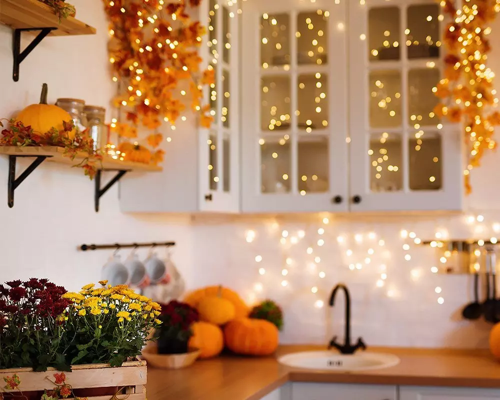 Pepco őszi konyhai dekoráció tökökkel, virágokkal és meleg fényű égősorokkal díszített fehér szekrényekkel.