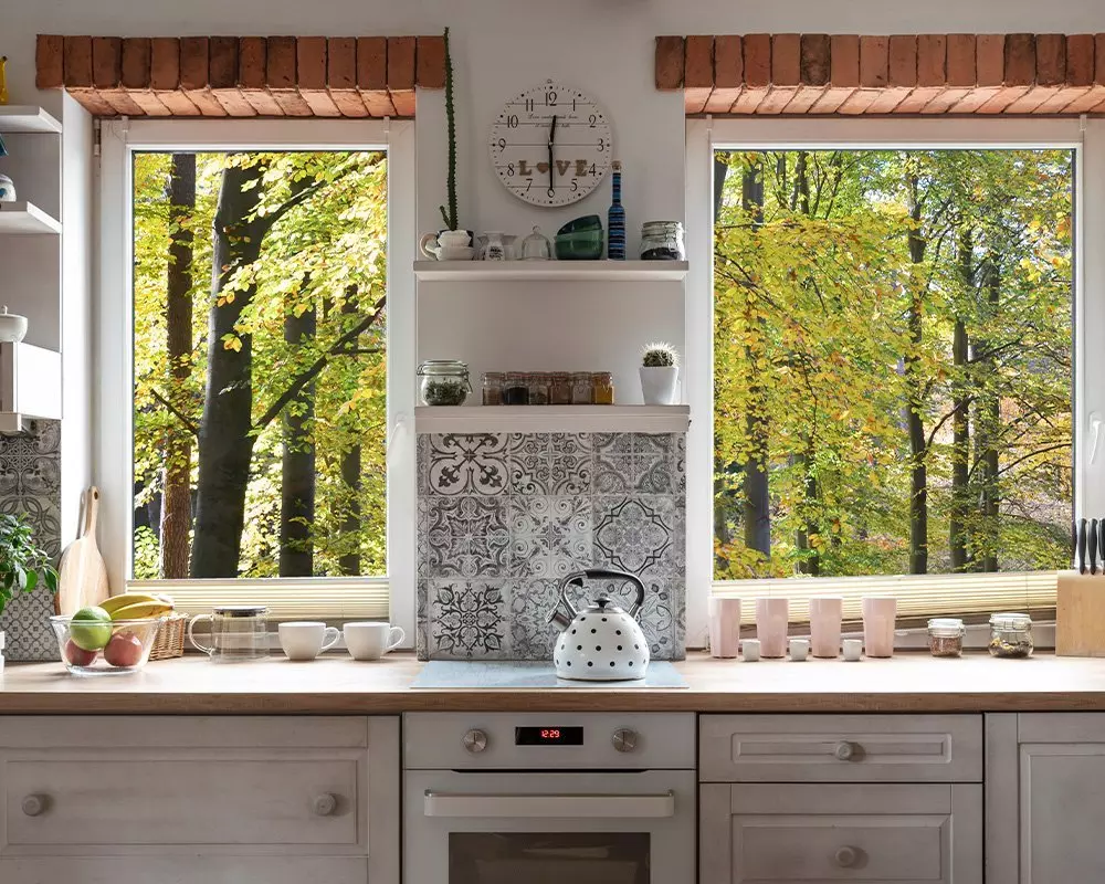 Przytulna kuchnia Pepco z dużymi oknami ukazującymi jesienne drzewa, białym czajnikiem w kropki i zegarem z napisem "Love".