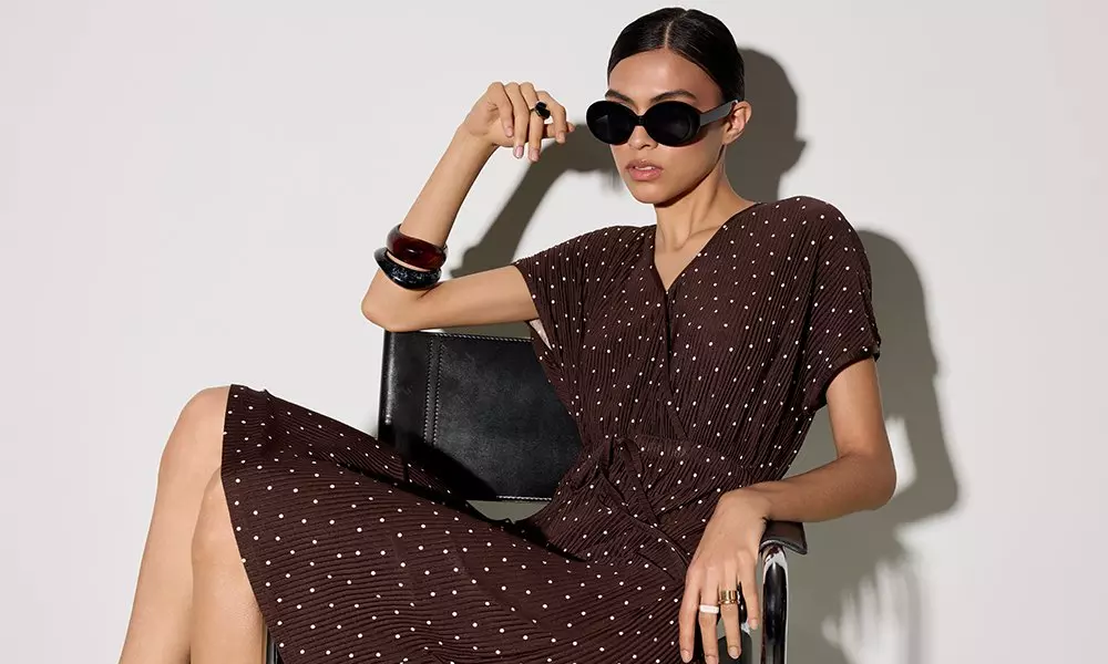 Pepco woman sitting wearing sunglasses, brown polka dot dress, bangles and holding a black handbag.