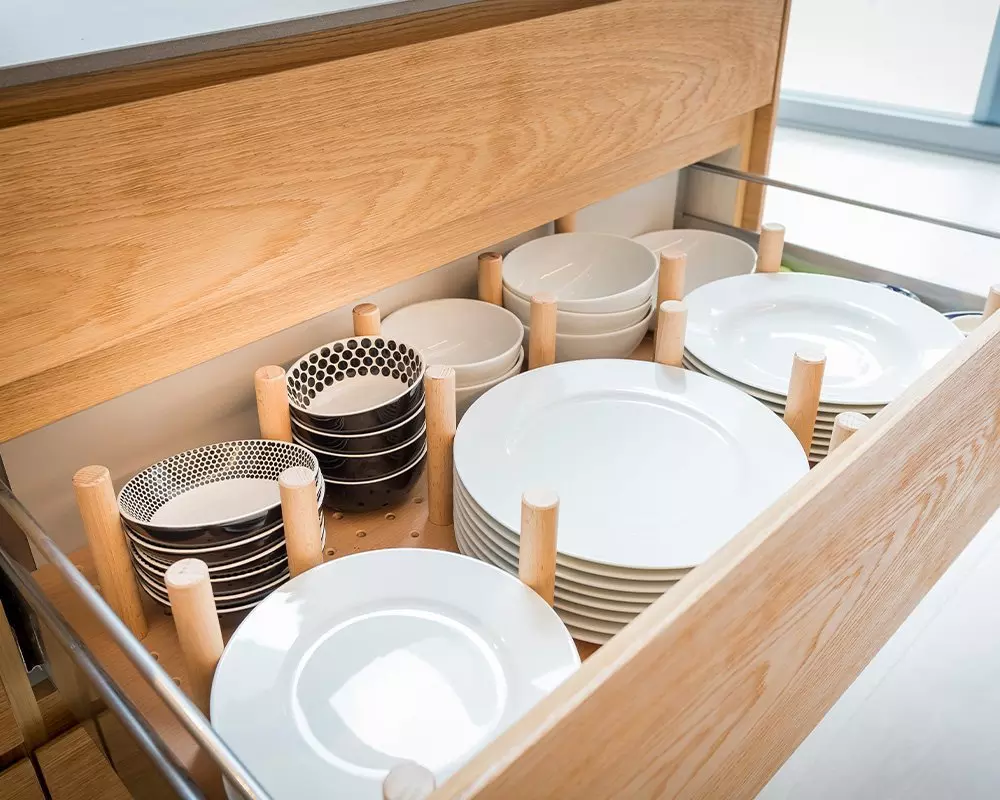 Drewniana szuflada kuchenna Pepco z organizerami na talerze, miski i naczynia w różnych wzorach i kolorach.