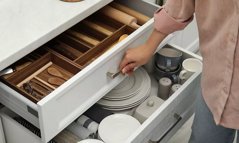 Osoba otwierająca szuflady kuchenne Pepco z drewnianym organizerem na sztućce oraz zastawą stołową w dolnej szufladzie.
