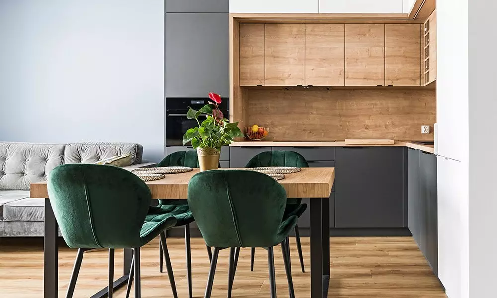 Modern konyha-étkező tér Pepco termékekkel, fa asztal körül zöld bársony székekkel és szürke kanapéval a háttérben.