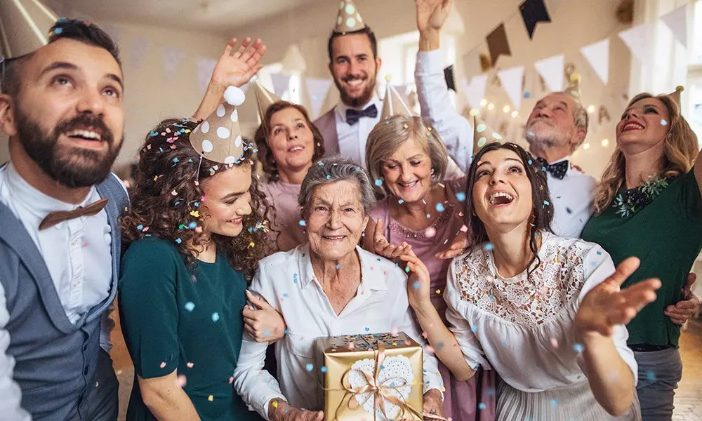 Group celebrating at a party with festive hats and decorations from Pepco, surrounding an elderly person holding a gift box.