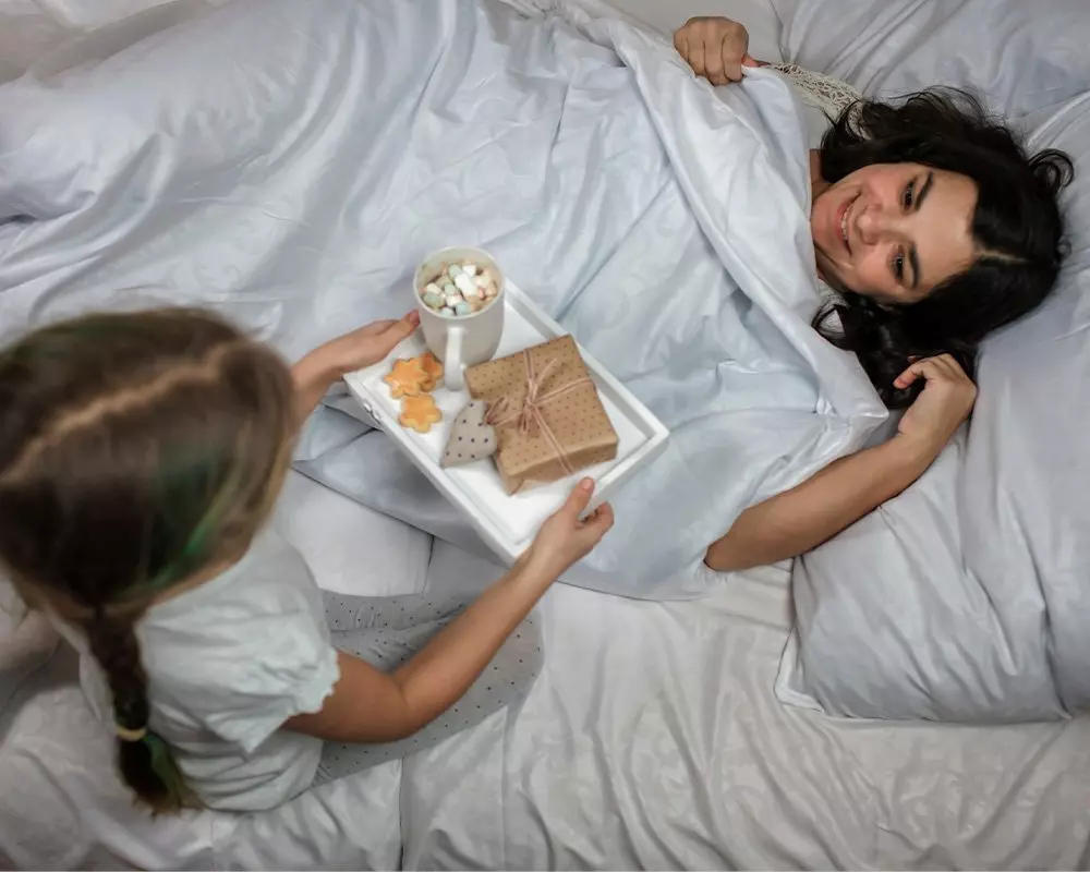 Osoba w łóżku otrzymuje tacę śniadaniową z prezentem, ciasteczkami i gorącym napojem z piankami od Pepco.