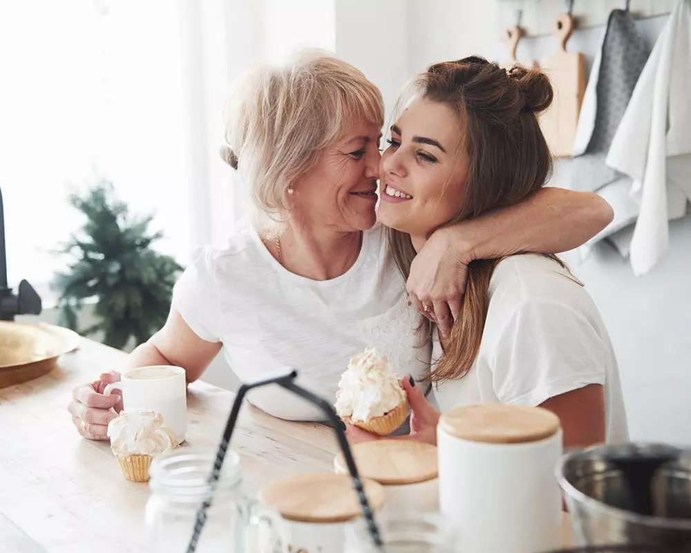 Dva lidé objímající se u stolu s cupcaky a nádobami od Pepco, v útulném kuchyňském prostředí s dřevěnými prvky.