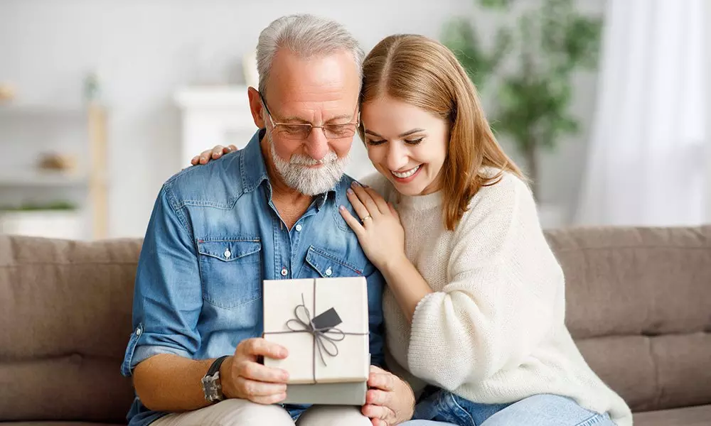 Älterer Mann und junge Frau betrachten gemeinsam ein Geschenk auf einem Sofa.