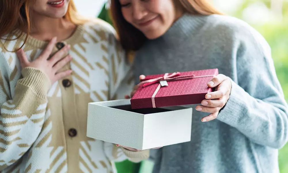 Dvě osoby v svetrech od Pepco otevírají dárkovou krabici s červeným víkem převázaným stuhou.
