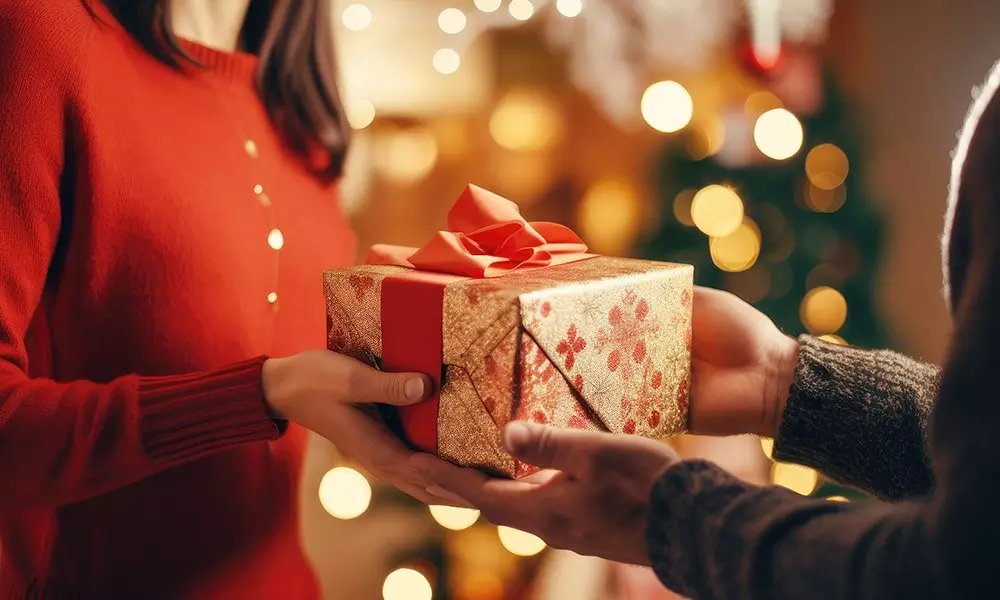 Person in red sweater receiving festive gold gift box with red ribbon from Pepco against warm holiday lights background.